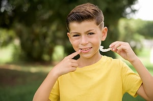 A kid holding an invisible aligner and pointing to her perfect straight teeth. Dental healthcare and confidence concept.
