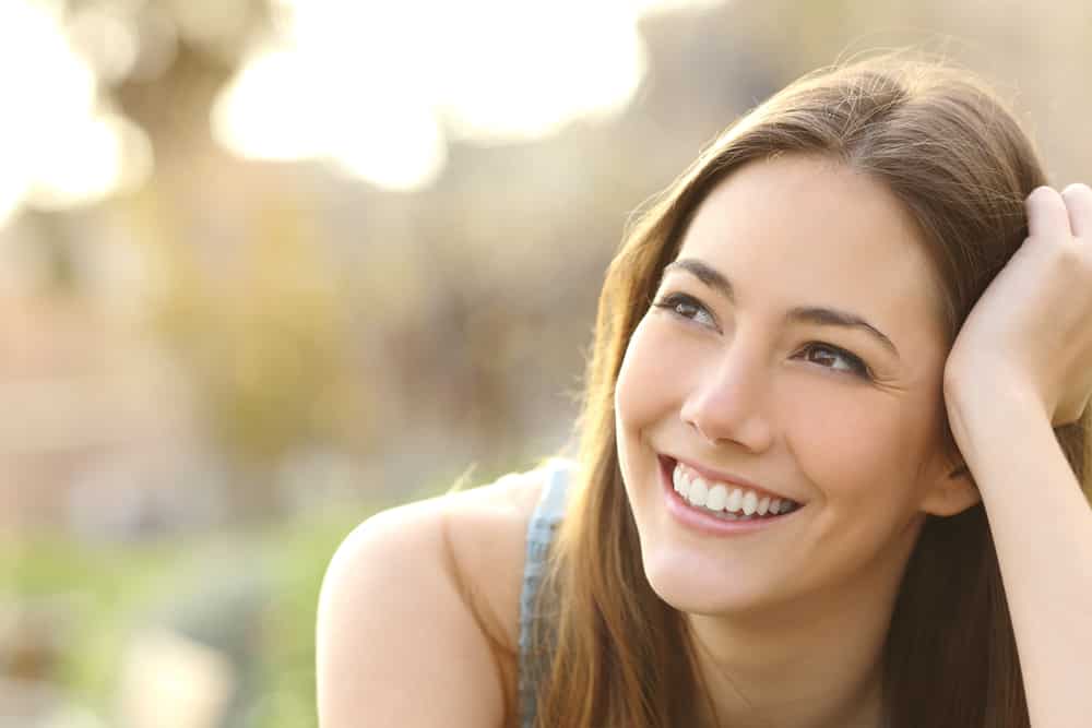 Woman with white teeth thinking and looking sideways in a park in summer